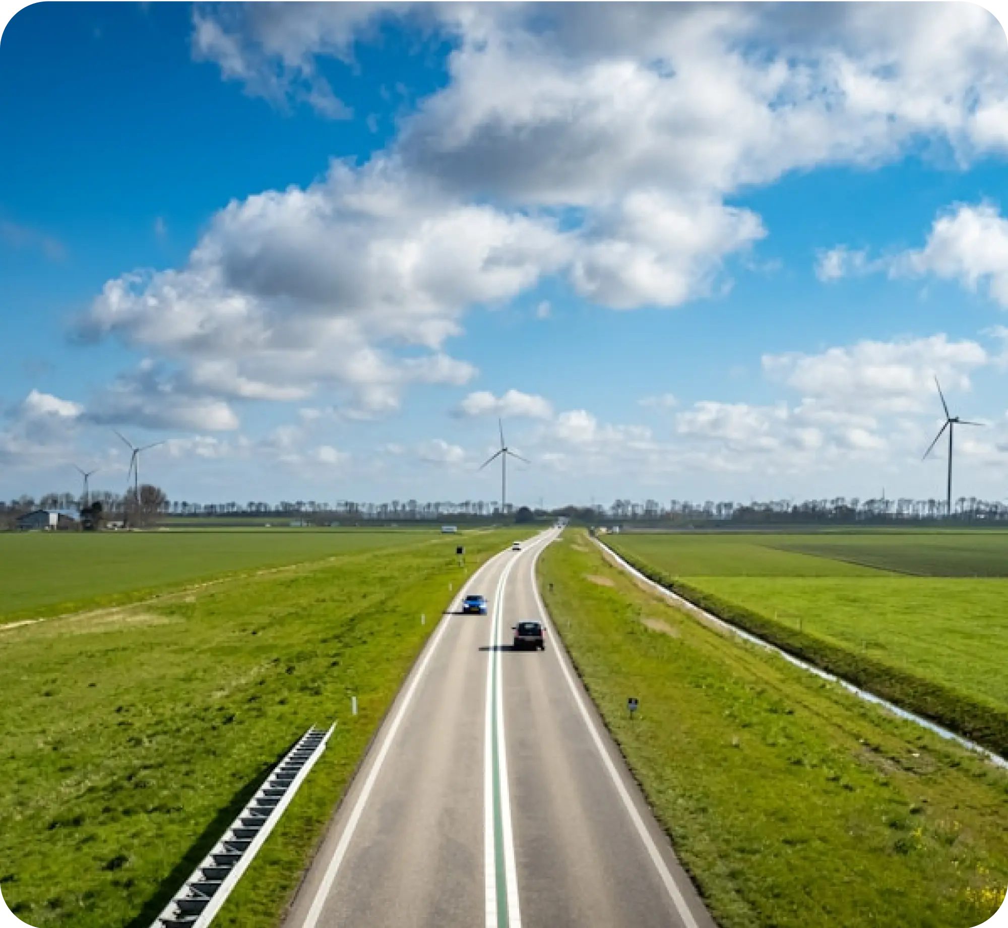 Rural highway through green fields with wind turbines on horizon.